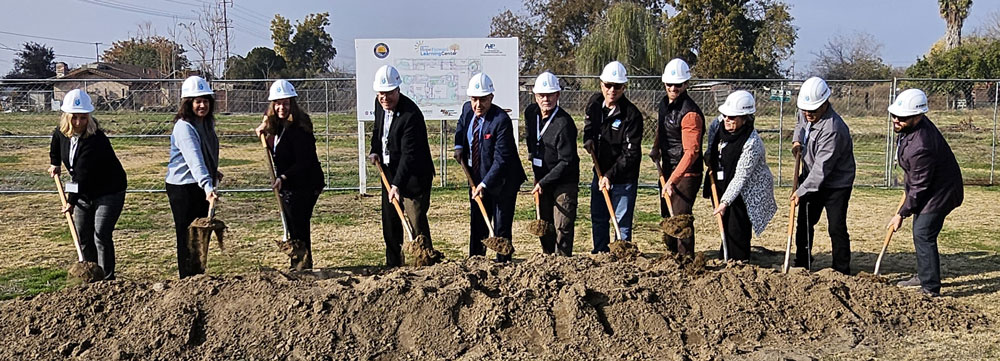 Groundbreaking for Central Valley TAY Independence Program. 11 people with white hard hats on digging in the dirt to break ground.