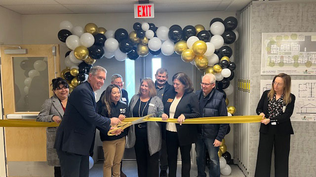 Ribbon Cutting for Walter's House. Group of people cutting a yellow ribbon.